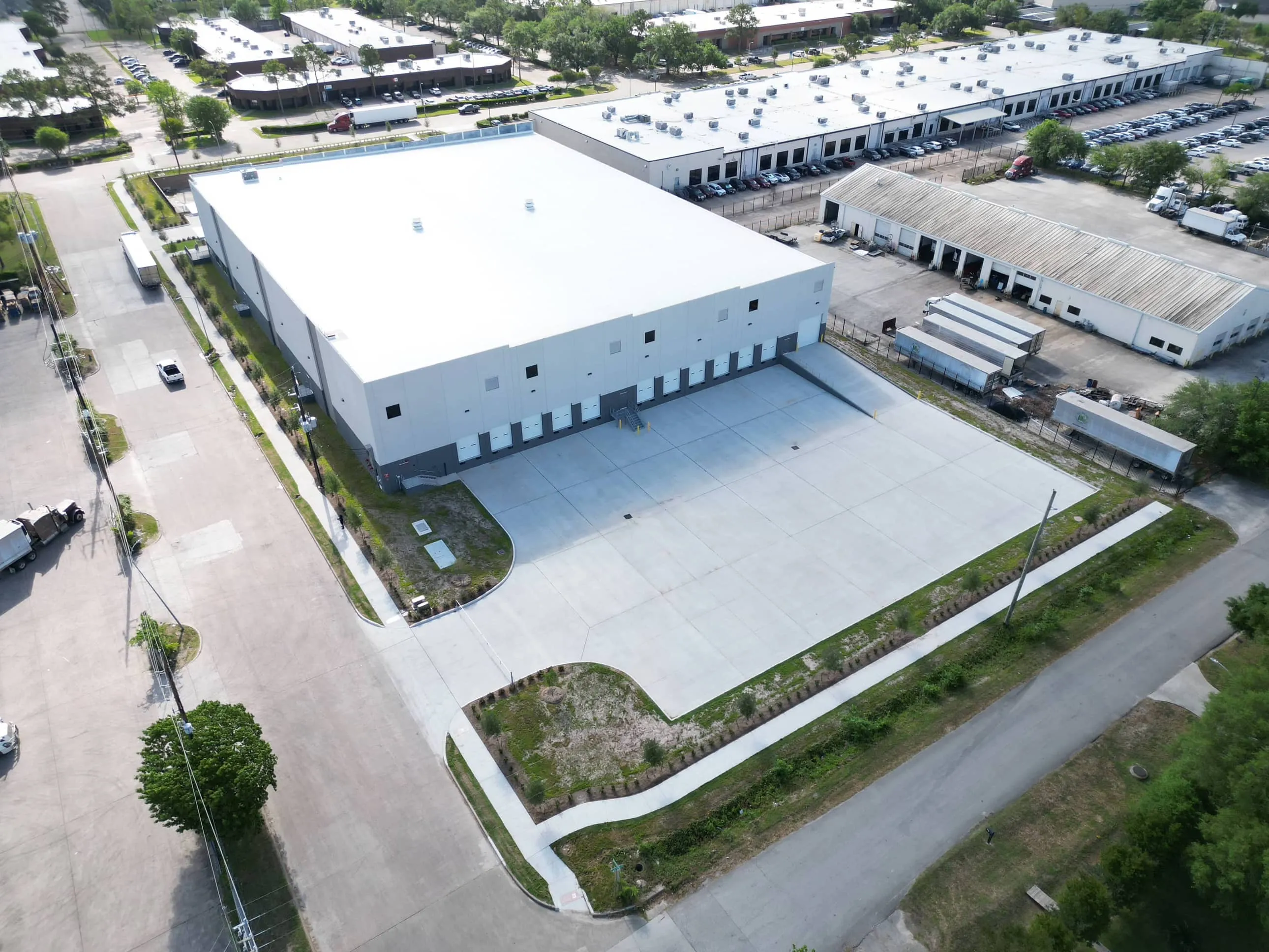 Aerial view of a white-roofed building and paved loading area at West X